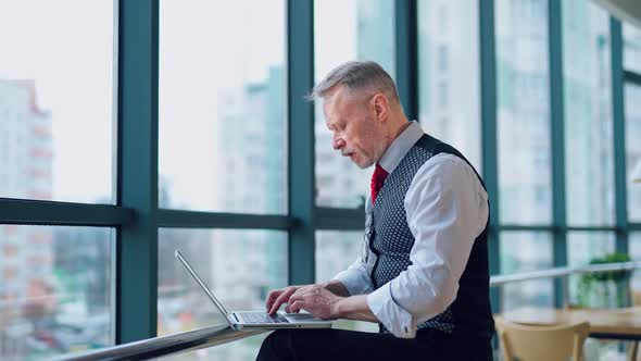 Thoughtful middle aged businessman in suit with a laptop sitting near the window working