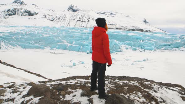 Young Woman Tourist in a Red Jacket Walks Around Huge Glacier in Iceland