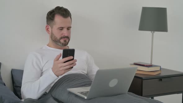 Man with Laptop Using Smartphone on Sofa