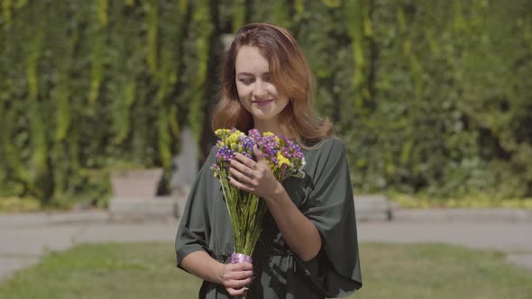 Portrait of Playful Cute Girl Sniffing Wild Flowers Looking at Camera While Standing Outdoors