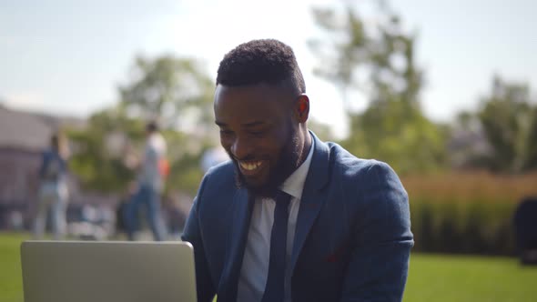 Young Smart African-american Businessman Doing Winner Gesture Working on Laptop in City Park