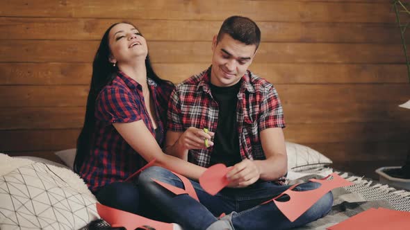 Handsome man is cutting out heart from the red paper for his girlfriend