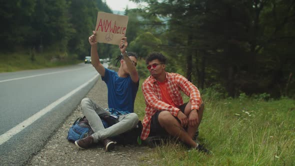 Handsome Multicultural Hipster Male Travelers Hitchhiking with Cardboard on Highway