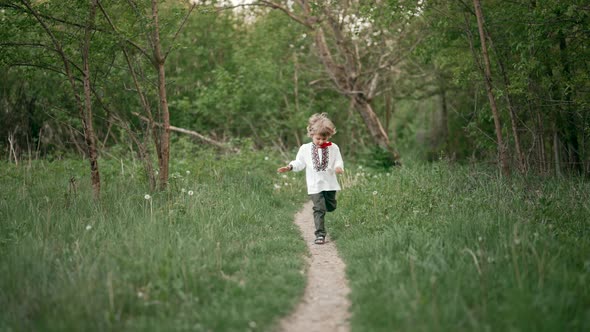 Little Ukrainian Boy Cheerfully Running Along Path on Forest Lawn or in Park