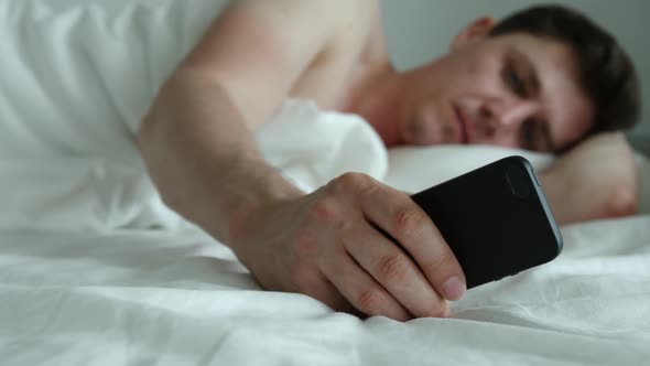 Young Adult Man Lies On A Bed And Uses Phone