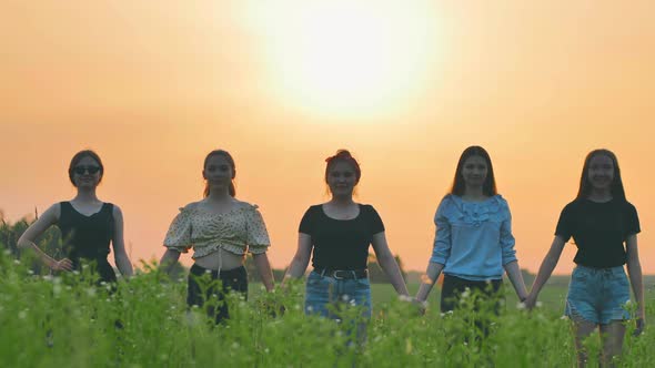 Girls Friends Waving Their Hands to the Setting Sun on the Background of the Sunset