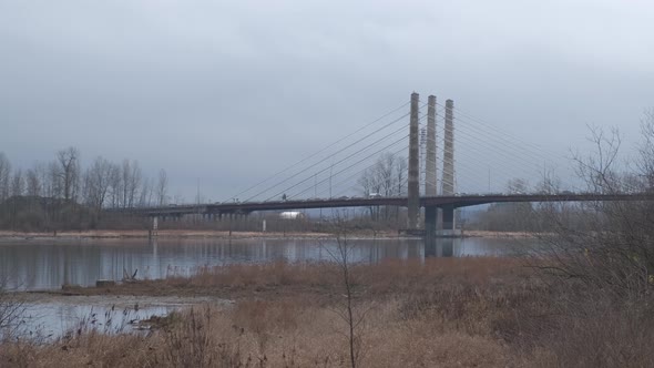 Local traffic on a bridge over a blue river with bare trees and fallen leaves on a cloudy day