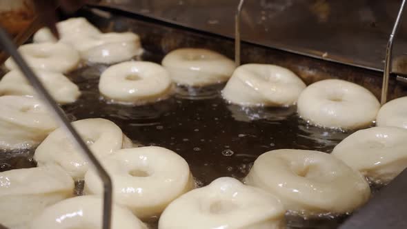 A cinematic close up of a bakers stick flipping a batch of fresh doughnuts in a homemade oil-filled