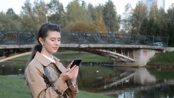 Beautiful Girl in a City Park Writes a Message on Her Phone