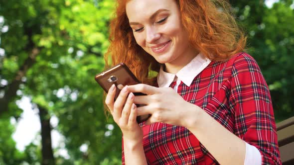 Red Haired Girl Texting Message on Smartphone in Green Park