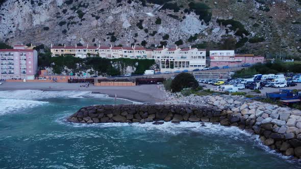 Turquoise Beach With Crashing Waves Onto Sea Walls On Catalan Bay In Gibraltar. Aerial Pullback