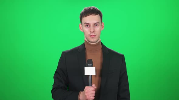 Man Reporter in Suit Looks Into the Camera and Speaks Into a Microphone on a Green Background a