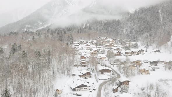 Drone shot descending through snowy ski village, snow flying towards the camera with low cloud, moun