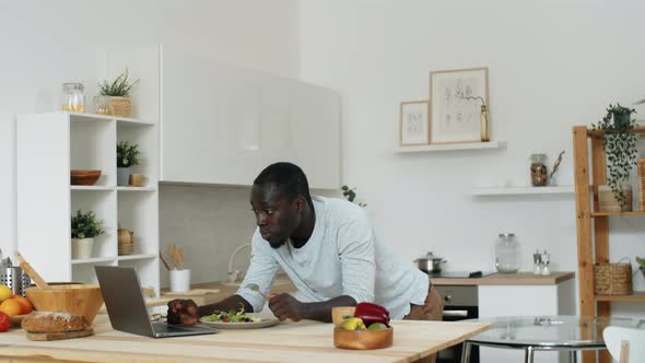 Afro-American Man Using Laptop and Eating Salad at Home