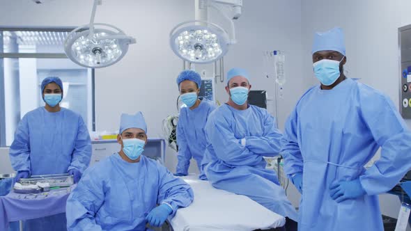 Diverse male and female doctors wearing face masks standing in operating theatre smiling to camera