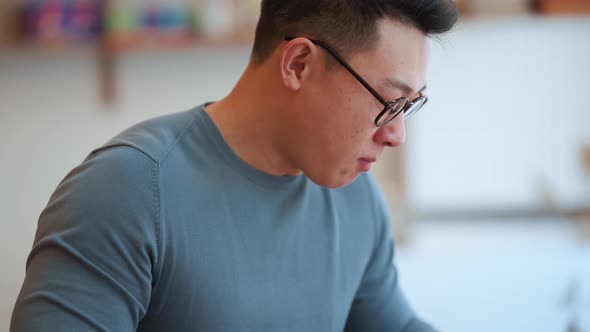 Smiling Asian young man wearing eyeglasses eating food