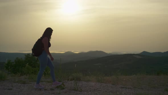 Happy Girl Tourist Walks on the Hillside with a Backpack