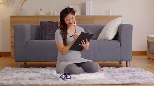 Asian pregnant woman writing checklist preparing for baby at home