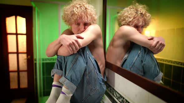 Portrait of Scared Queer Person Sitting in Bathroom Looking Over Shoulder at Reflection in Mirror