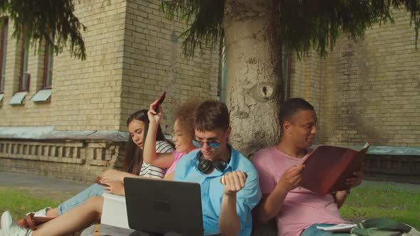 Closeup of Students Studying Using Gadget Sitting Under Tree Outdoors