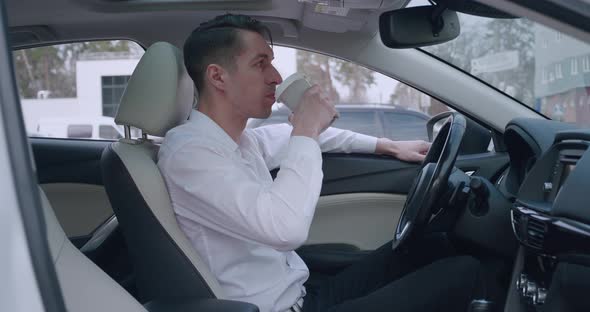 Portrait of Young Man Businessman in White Shirt Sitting in the Car and Drinking Coffee