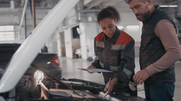 Female Auto Mechanic Talking to Client and Inspecting Car
