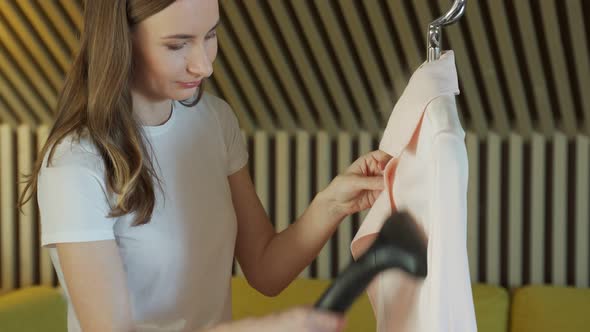 Woman Ironing Raincoat with Garment Steamer at Home