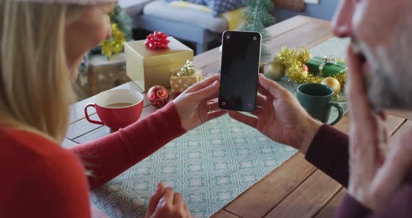 Happy caucasian mature couple wearing santa hats using smartphone with copy space