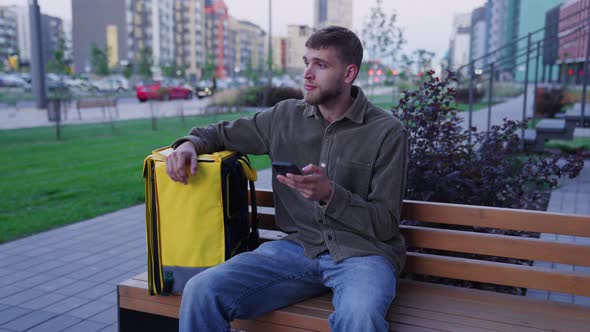 A Tired Courier Sits Down on a Bench Near the Entrance