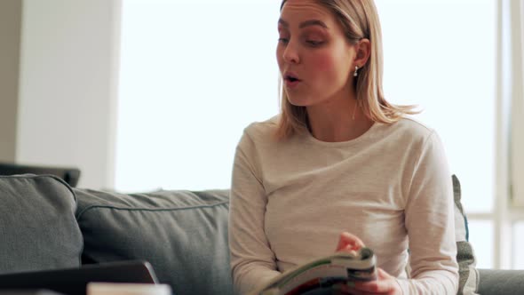 Concentrated blonde woman working on laptop and reading something from magazine