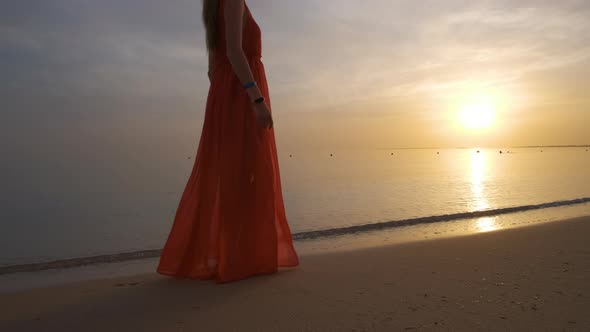 Young Woman in Red Dress Walking Alone on Sandy Beach By Seaside Enjoying Warm Tropical Evening