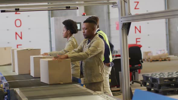 Diverse male and female workers with boxes on conveyor belt in warehouse