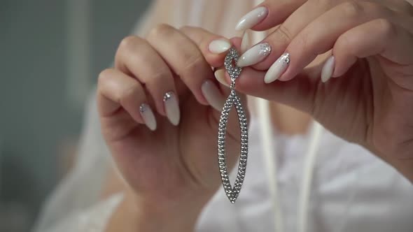 Girl holds and puts on an earring. Bride dresses on morning of her wedding day.