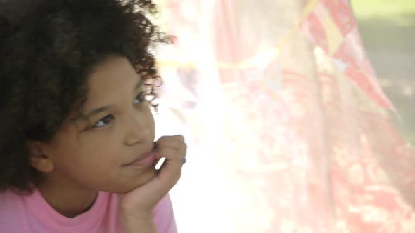 Girl in a play tent, thinking and looking at camera