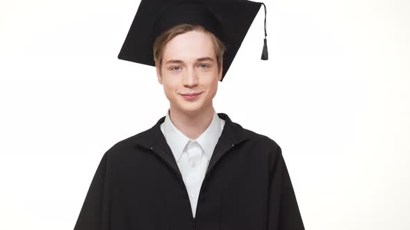Young Caucasian Male Graduate in Black Robe and Square Academic Cap Standing on White Background