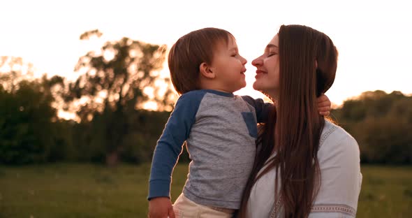 The Son Kisses His Mother Sitting at Sunset in a Field Hugging and Loving Mother