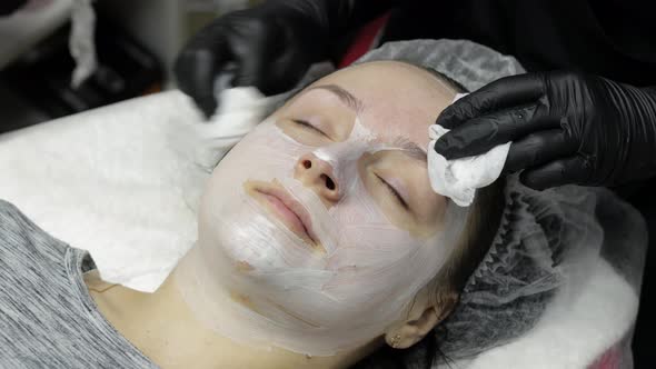 Cosmetologist Clean Clien Woman Face From Moisturizing Mask in Beauty Salon