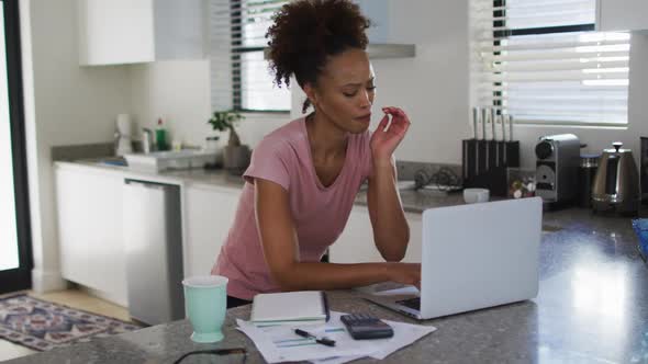 Mixed race woman in kitchen using laptop