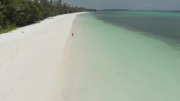 Aerial: Woman walking on white sand beach turquoise water tropical coastline Pas