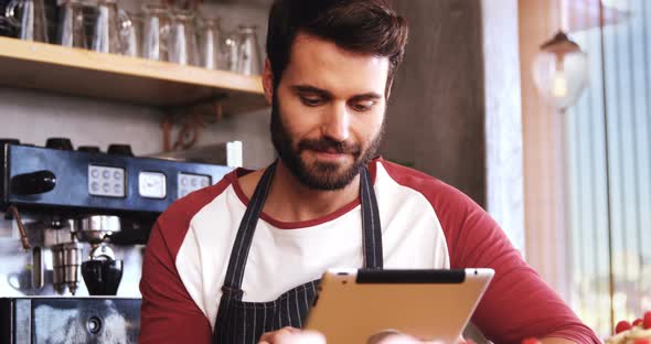 Smiling waiter using digital tablet at counter in cafe