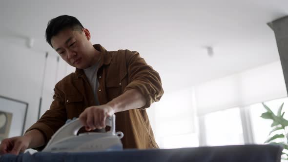 Positive Asian man ironing clothes