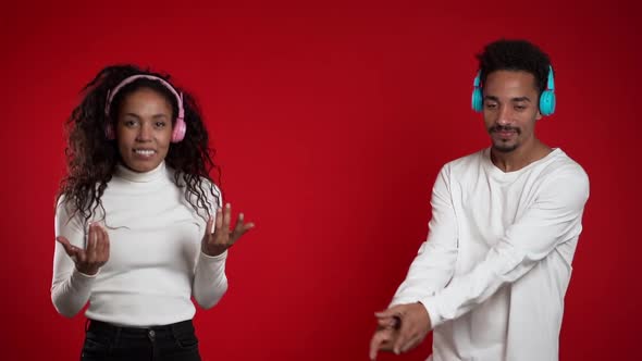 Young African American Couple Dancing with Headphones Isolated on Red 