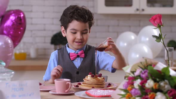 Happy Toddler Boy Pouring Maple Syrup on Pancakes