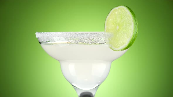 Classic Margarita cocktail on green background, rotate. Glass with a cocktail