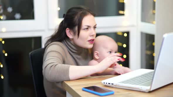 Young Woman with Toddler in Arms Typing on Laptop Remote Work with a Baby at Home