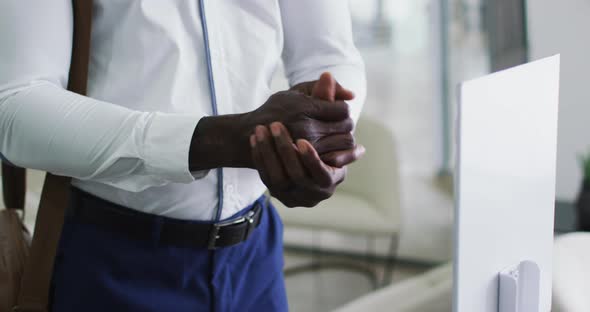 African american businessman in face mask disinfecting hands upon arrival in office