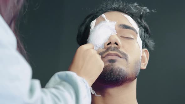 Make up artist putting white prosthetic insert on man's eye and making a Halloween mask