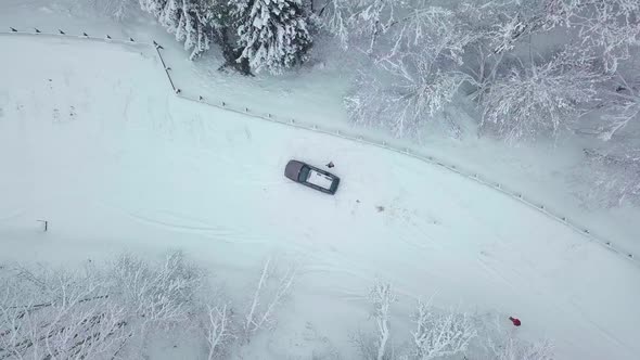 woman waves her hand and a car in winter in the forest. drone flies up.