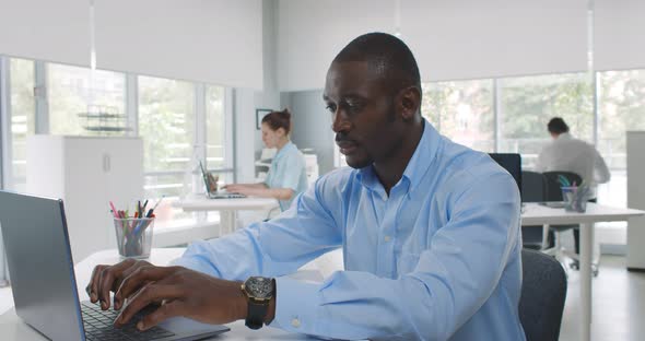 Concentrated African Businessman Typing on Laptop in Office Smiling at Camera