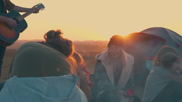 People Rest Listening To Guitar By Camp Bonfire at Sunset